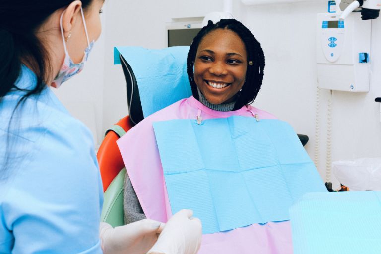 Patient with full set of teeth smiling in dental attire in clinic at dental staff member